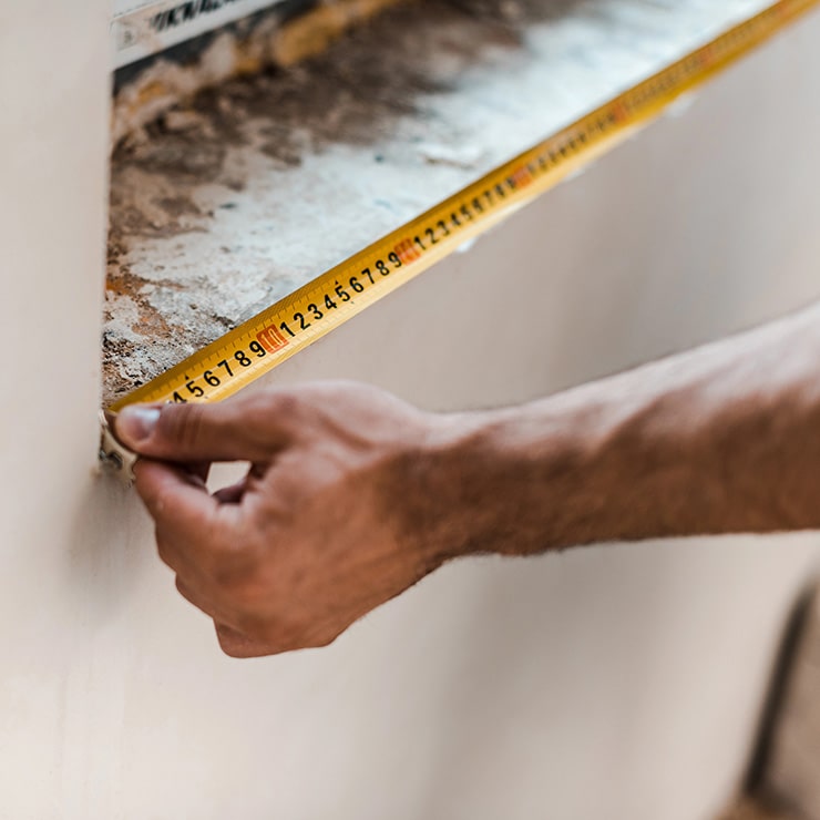A person's hand holding a yellow measuring tape against a rough, unfinished surface during construction.