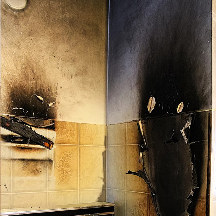 A corner of a room showing extensive fire damage, with black soot covering the walls and peeling paint.