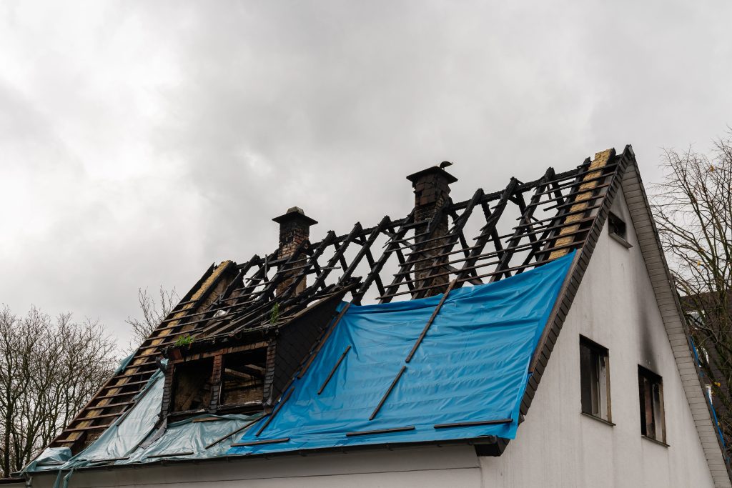 Fire-damaged house roof with exposed rafters and blue tarp covering