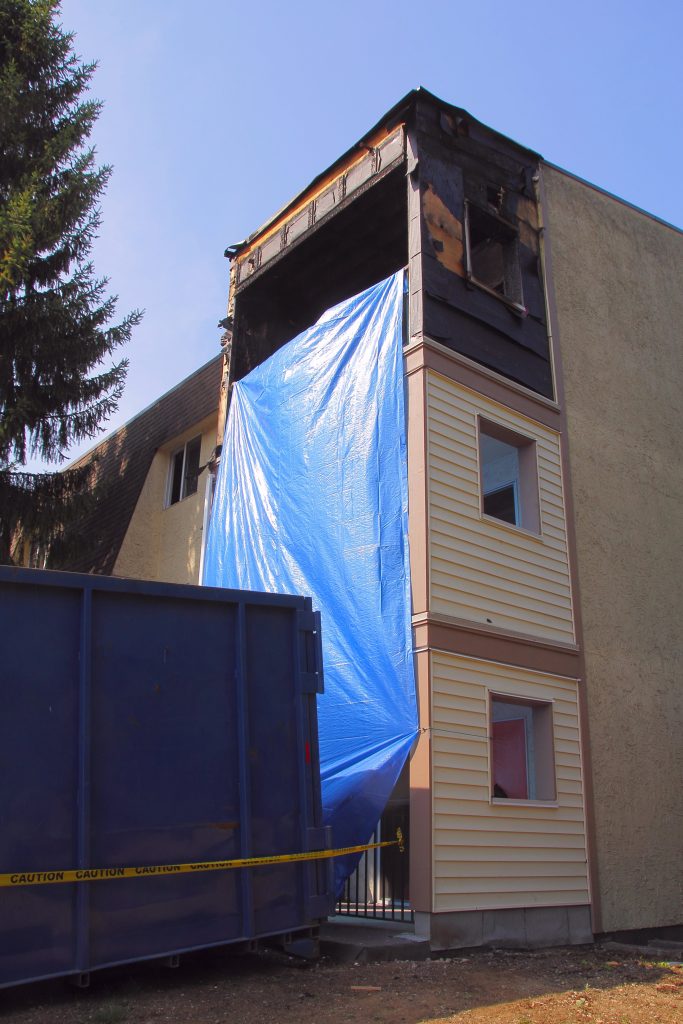 Residential building with fire damage covered by blue tarp and a dumpster