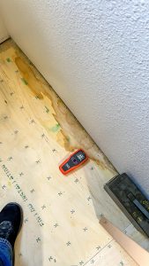 Moisture meter on wet plywood subfloor detecting water damage