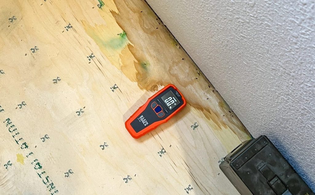 Moisture meter on wet plywood subfloor detecting water damage
